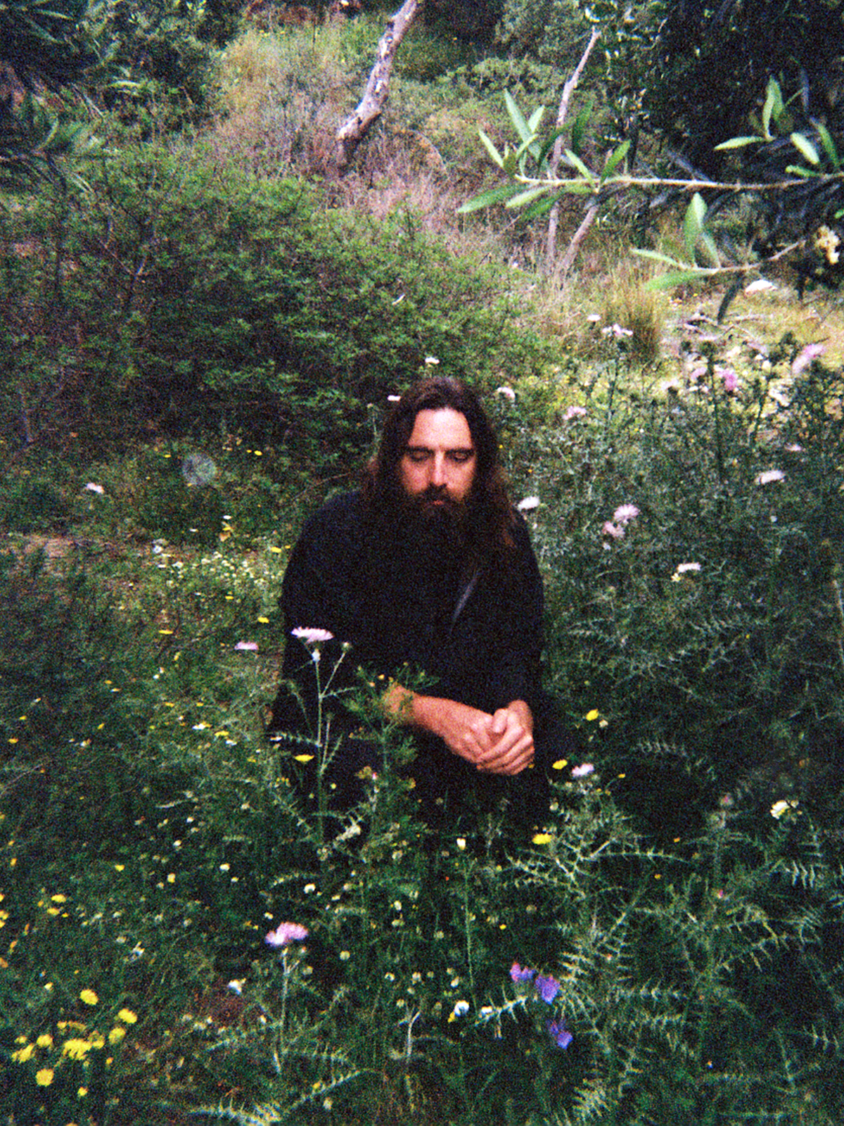 A photo of John Also Bennett crouching in a lush green garden